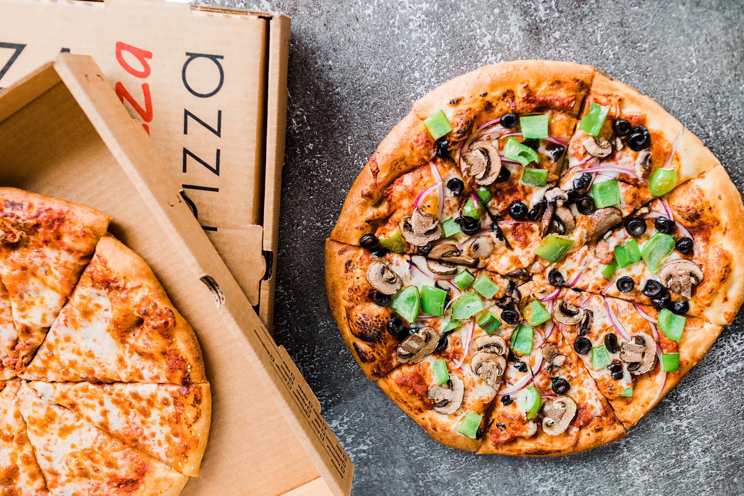 A cheese pizza in a box and a deluxe pizza. on the counter at Doryland Pizza