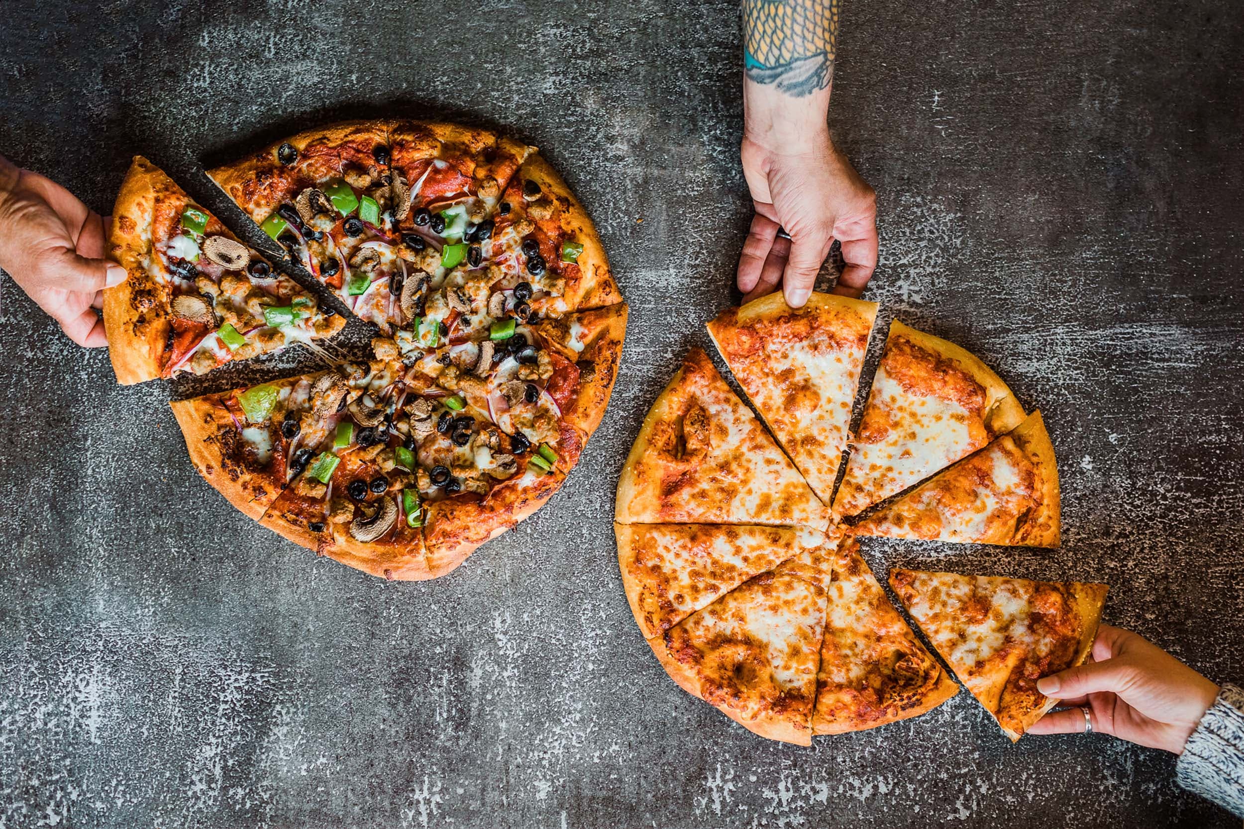 3 hands grabbing a slice of Dorlylands cheese and deluxe pizza