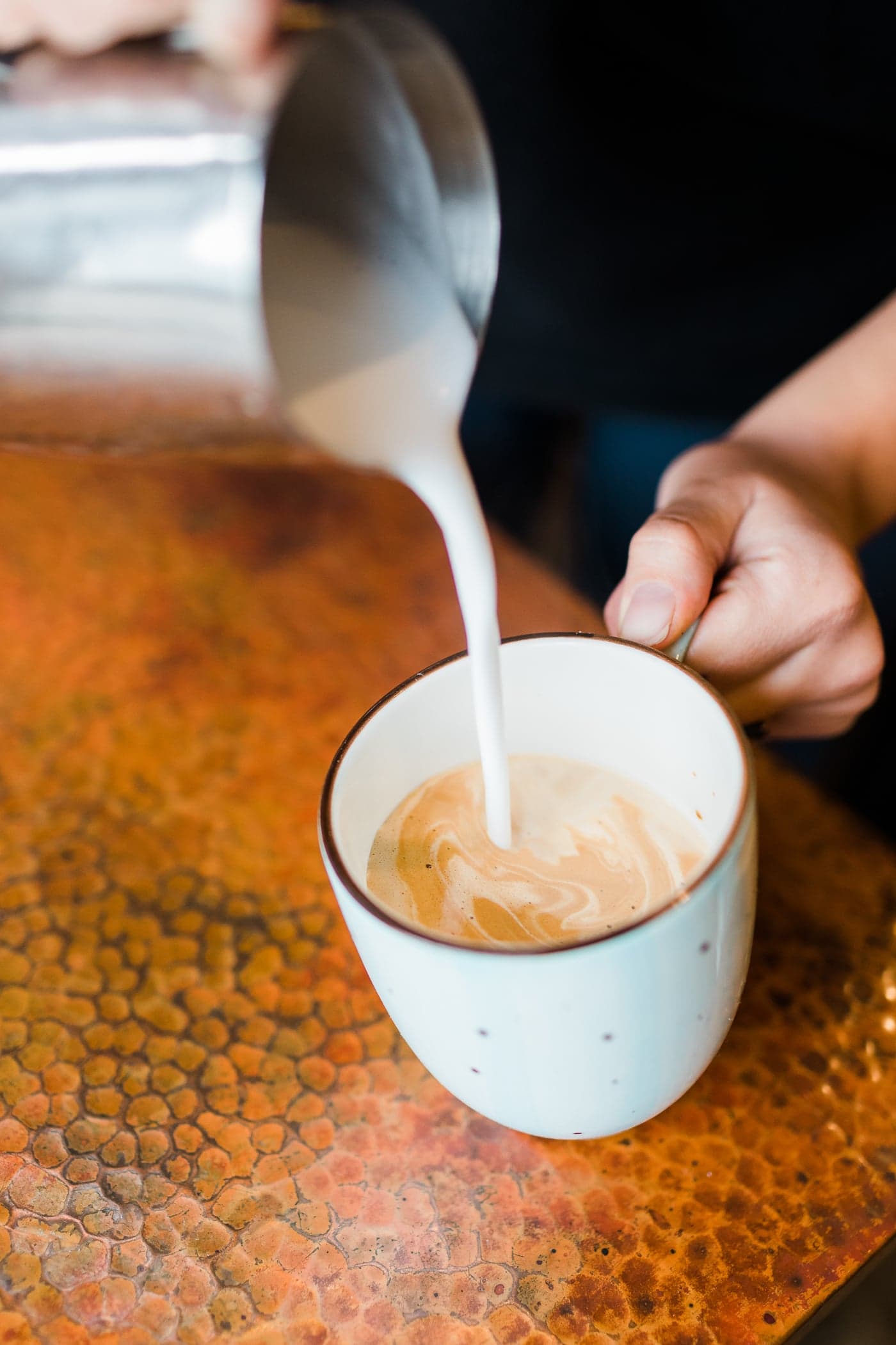 a barista pouring steamed milk into coffee