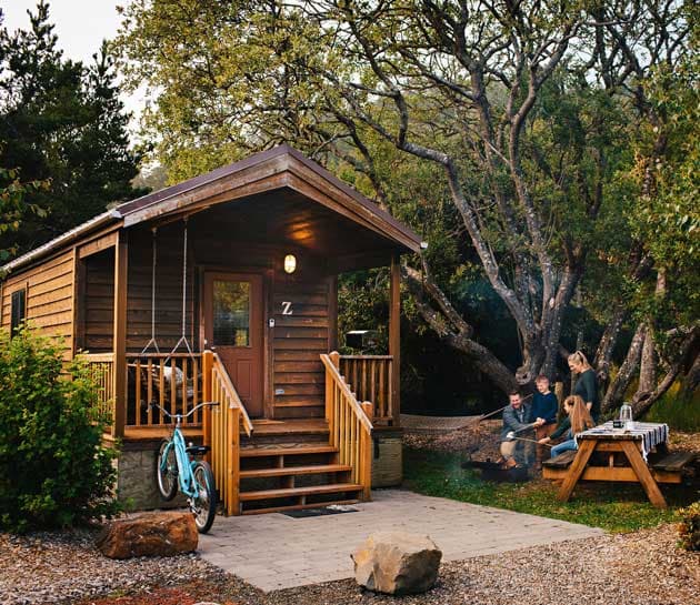 A family roasting marshmallows in a fire pit outside a cabin at Harts Camps