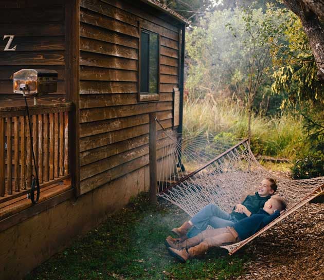 Two children laying on a hammock outside a cabin at Harts Camp
