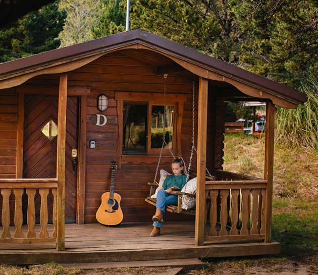 A child reading a book on the swing on the front porch of a cabin at Harts Camp