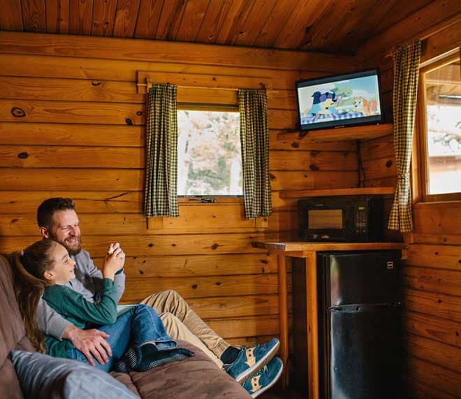 A father and daughter watching TV in a cabin at Harts Camp