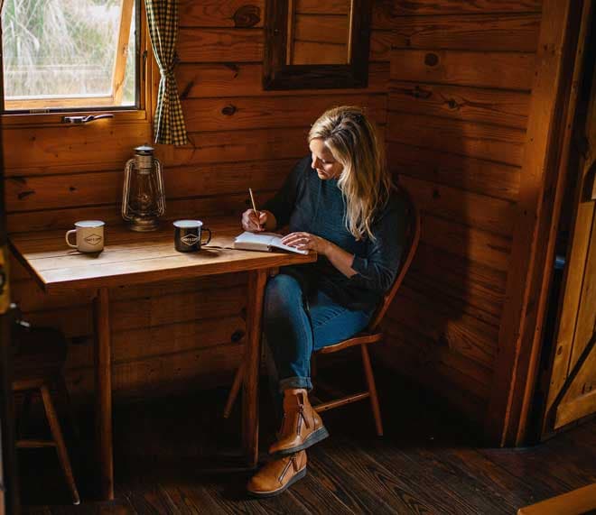 A woman writing in a book at the table inside a cabin at Harts camp