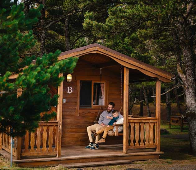 A father and son hanging out on the porch swing at a cabin at Harts Camp
