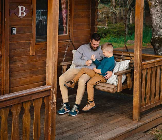 A father and son playing rock, paper, scissors on the porch swing of a cabin at Harts Camp