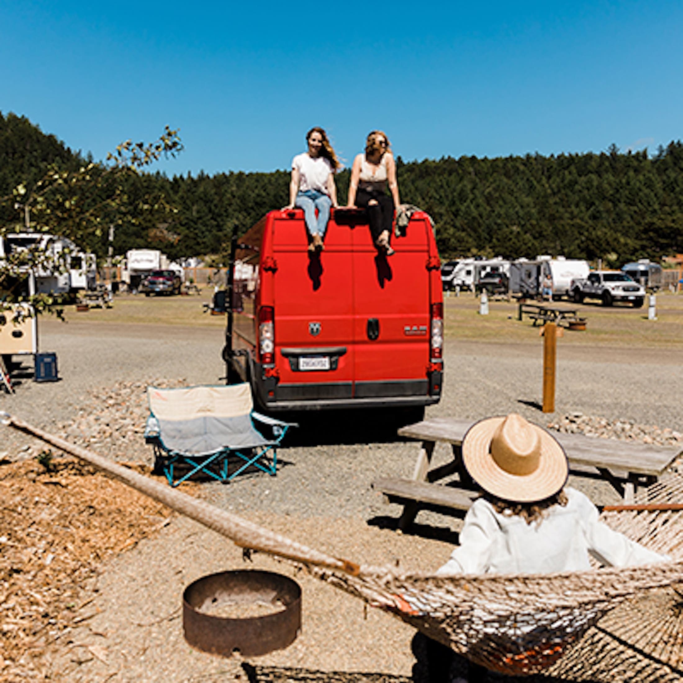 Two women sitting on top of a red van at a van site at Hart's Camp, Pacific City
