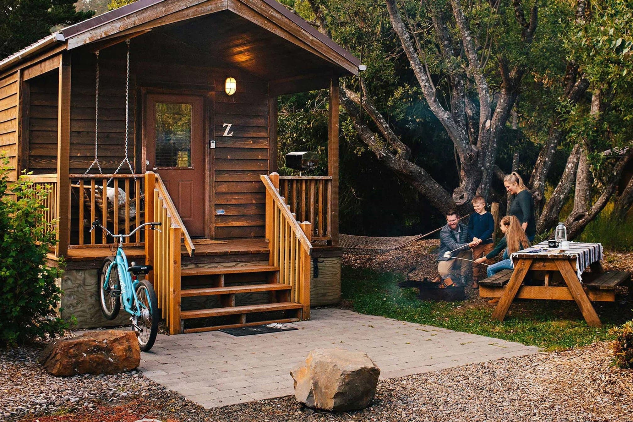 The exterior of a cabin at Hart's Camp with a family roasting marshmallows around a fire pit