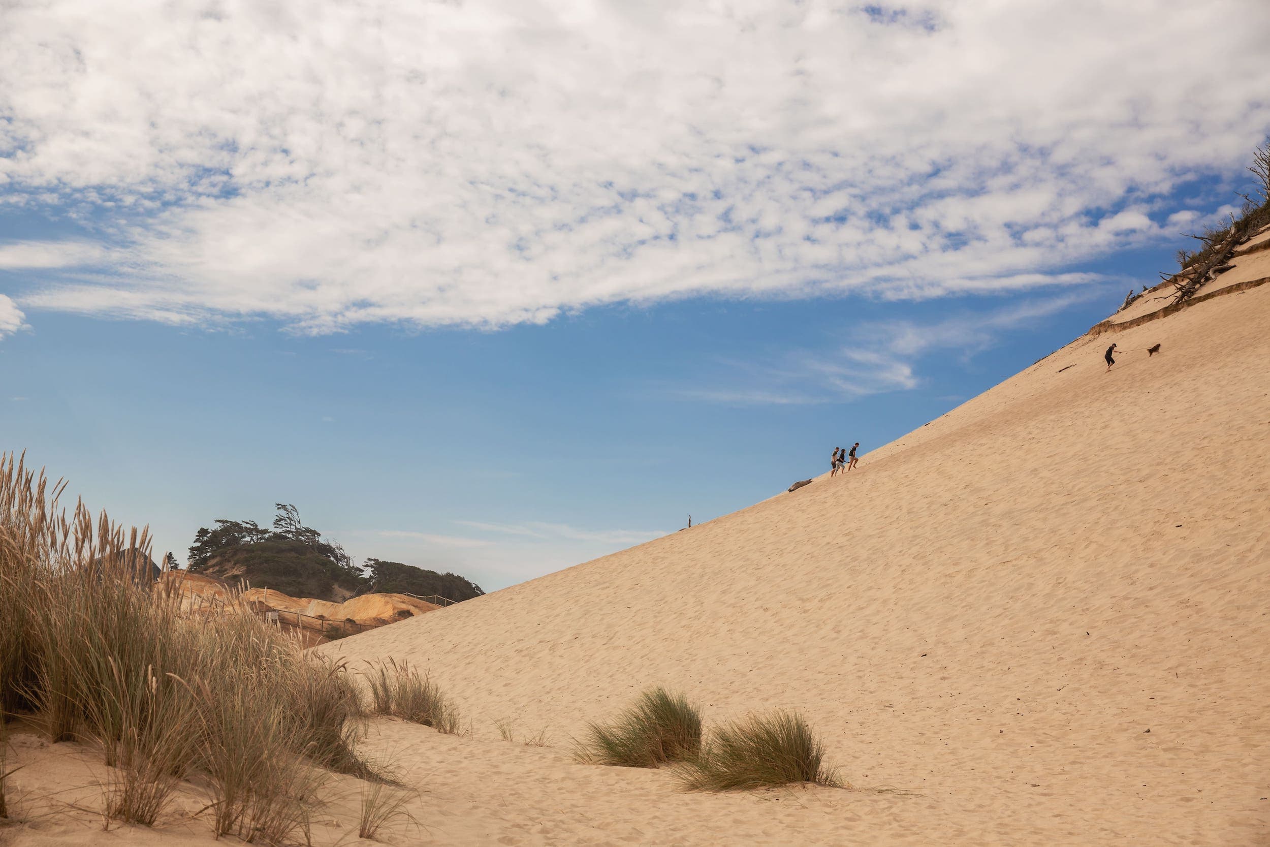 Three people walking up a sand dune at Cape Kiwanda