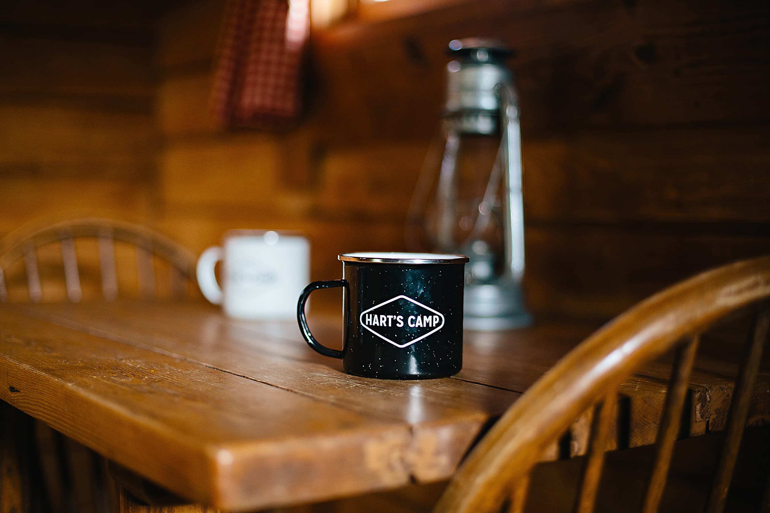 Hart's Camp enamel camp mug and vintage lantern on a rustic cabin table, capturing cozy glamping comfort at The Inn at Hart's Camp in Pacific City on the Oregon Coast.