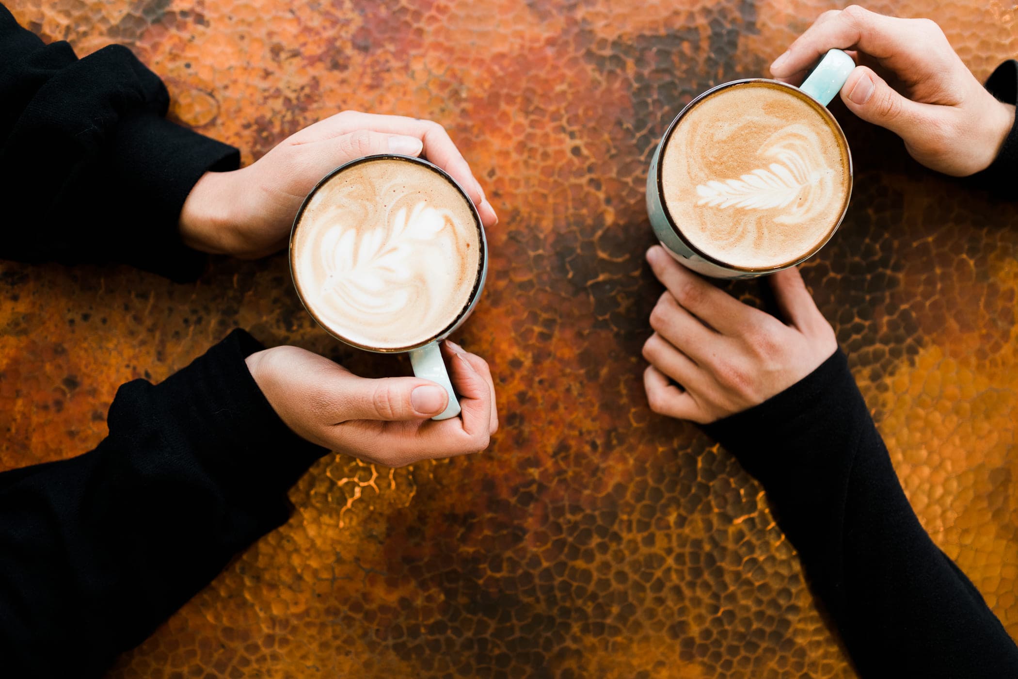 Two people holding a cappuccino on a table at Stimulus Coffee