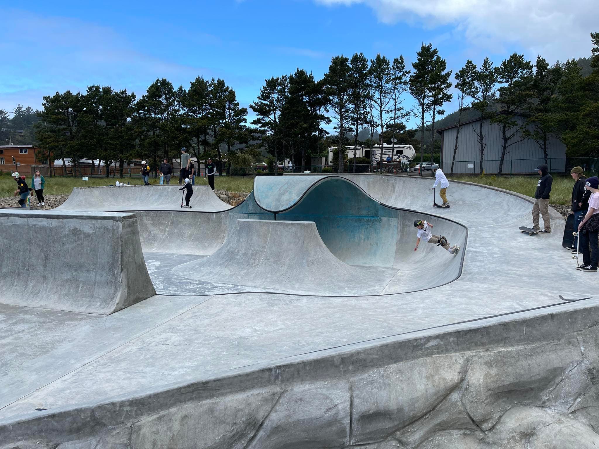 A bunch of kids skateboarding and scootering at the Pacific City Skatepark
