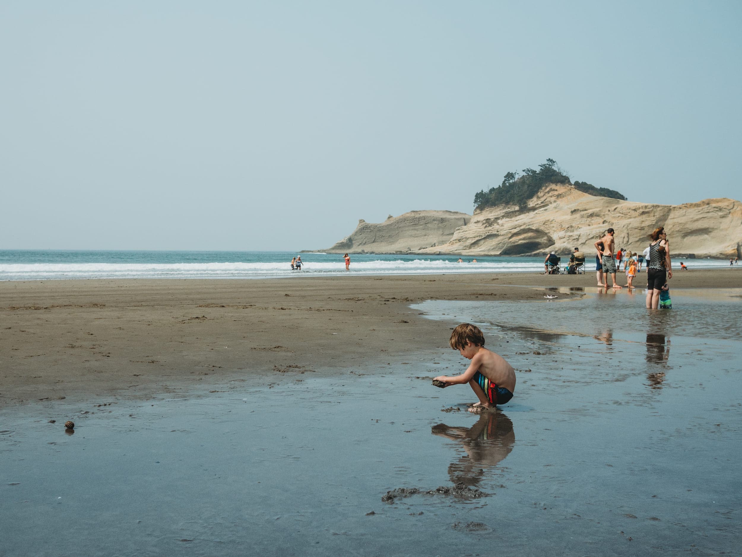 A little boy making mud pies on a beach with vacationers in the background