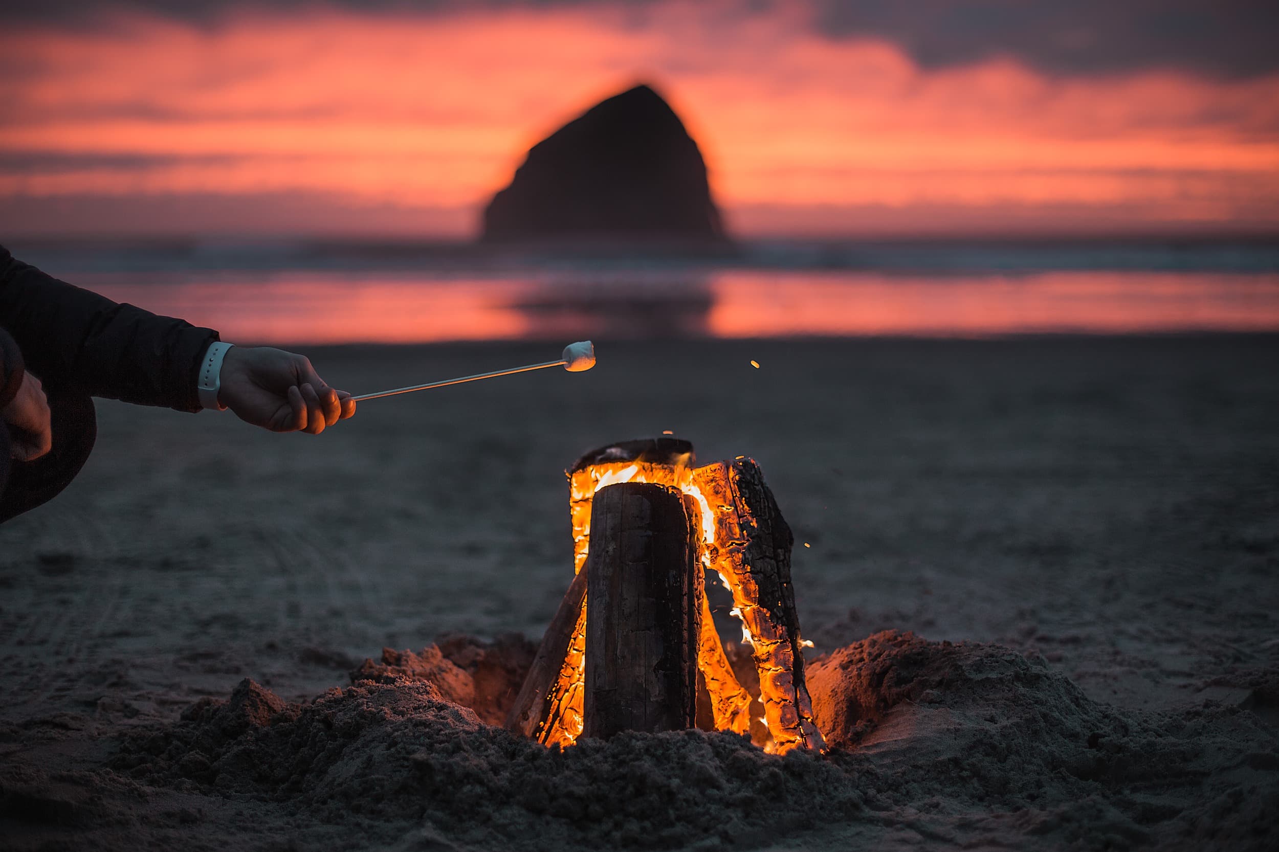 Roasting marshmallows over a beach bonfire at sunset with Pacific City's Haystack Rock at Cape Kiwanda, steps from Hart's Camp on the Oregon Coast
