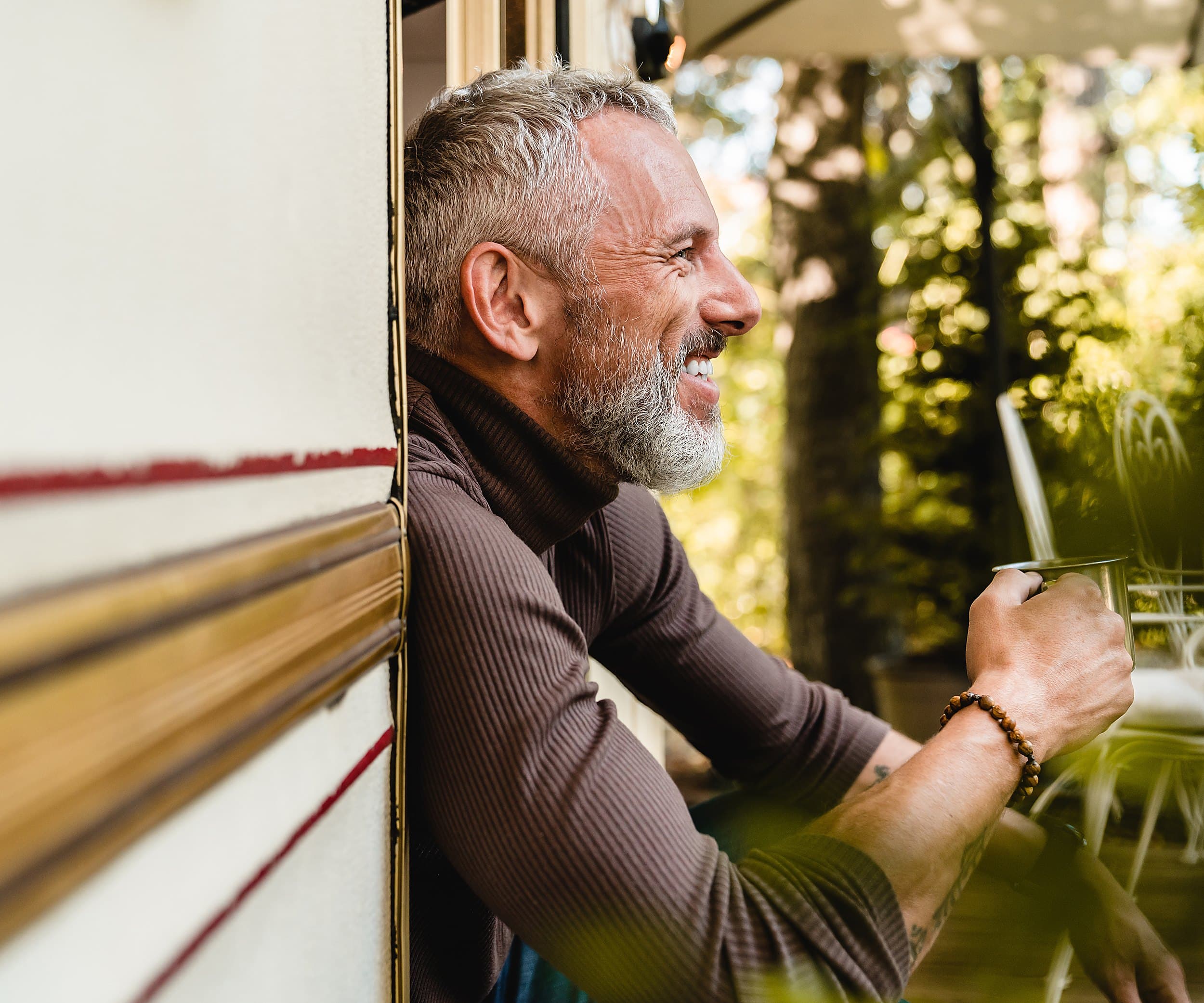 Guest enjoying morning coffee in the doorway of an Airstream surrounded by coastal pines at Hart's Camp Pacific City Oregon