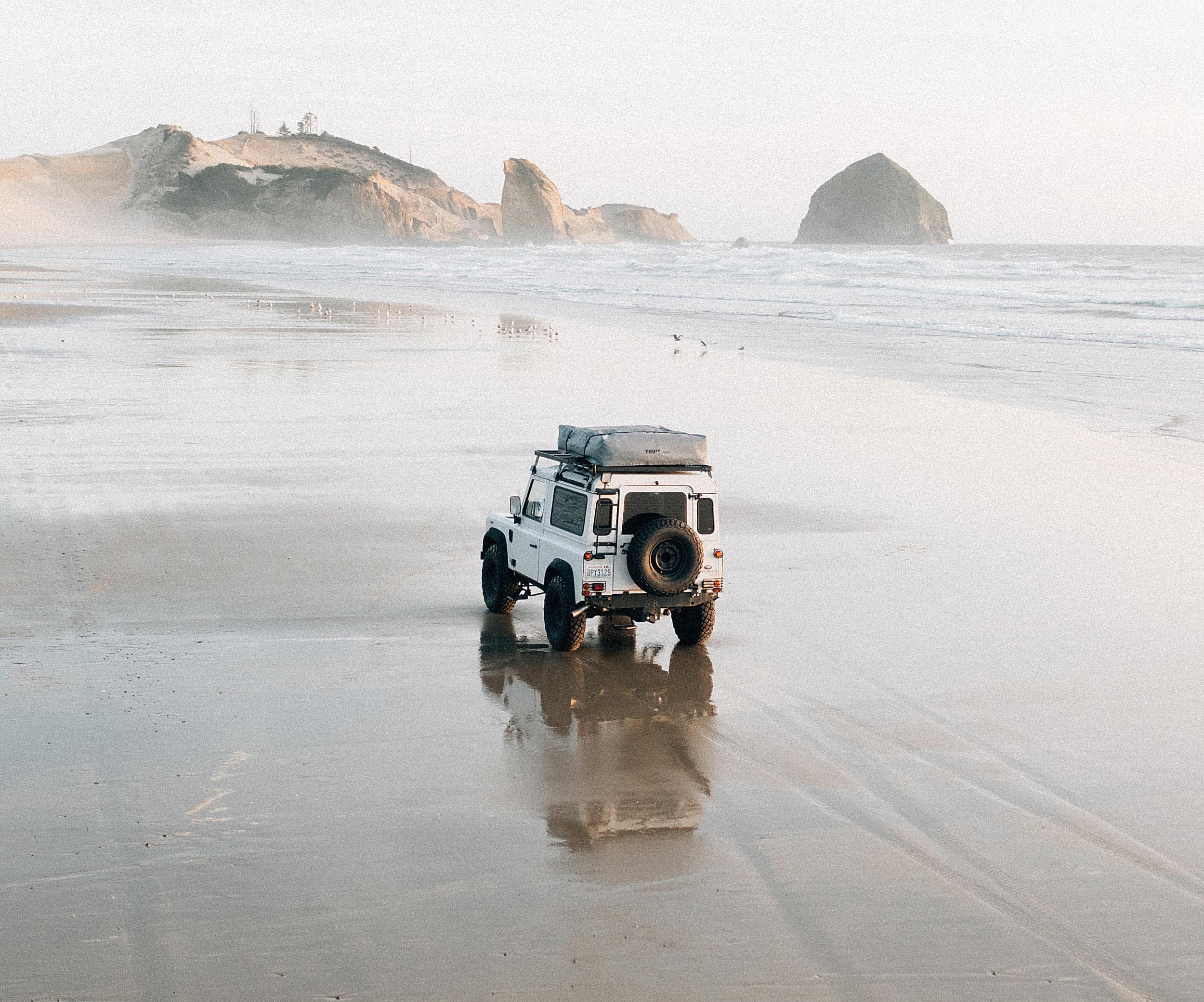 Overland 4x4 parked on the sand at Cape Kiwanda with Haystack Rock in the distance, near The Inn at Hart's Camp in Pacific City, Oregon.