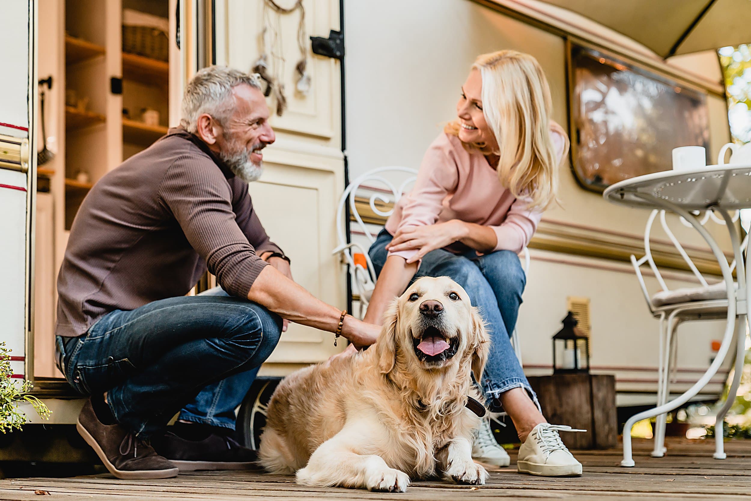 Couple relaxing with their golden retriever beside an RV awning, reflecting the pet-friendly RV camping at The Inn at Hart's Camp