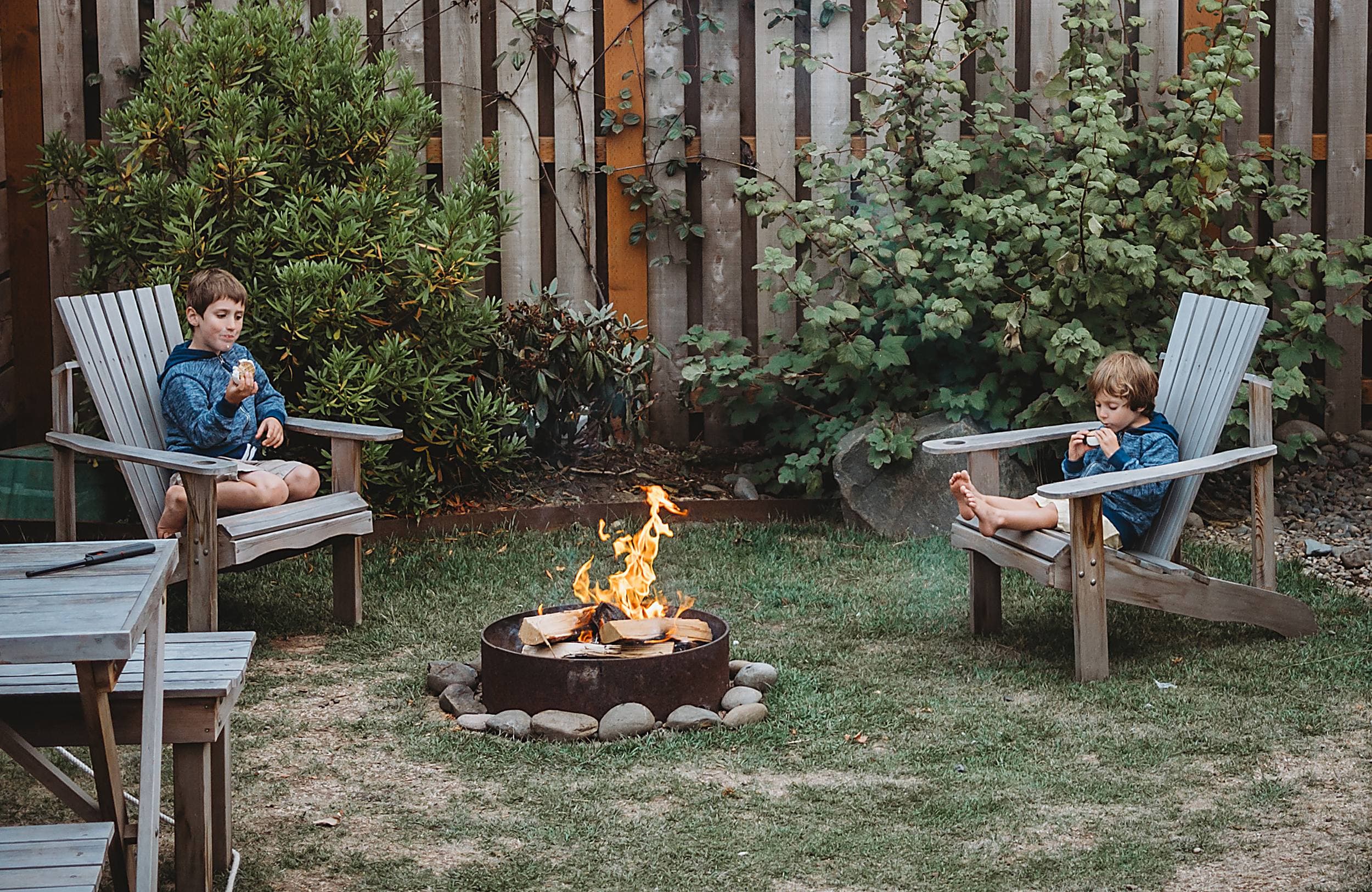 Two children roasting s'mores by a glowing fire pit in Adirondack chairs at The Inn at Hart's Camp, a pet-friendly glamping resort in Pacific City on the Oregon Coast near Cape Kiwanda