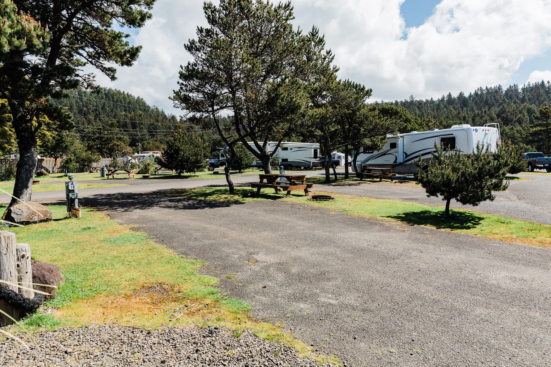 Shore pine–shaded RV site with picnic table and fire ring at the Hart's Camp RV park, minutes from Cape Kiwanda in Pacific City, Oregon