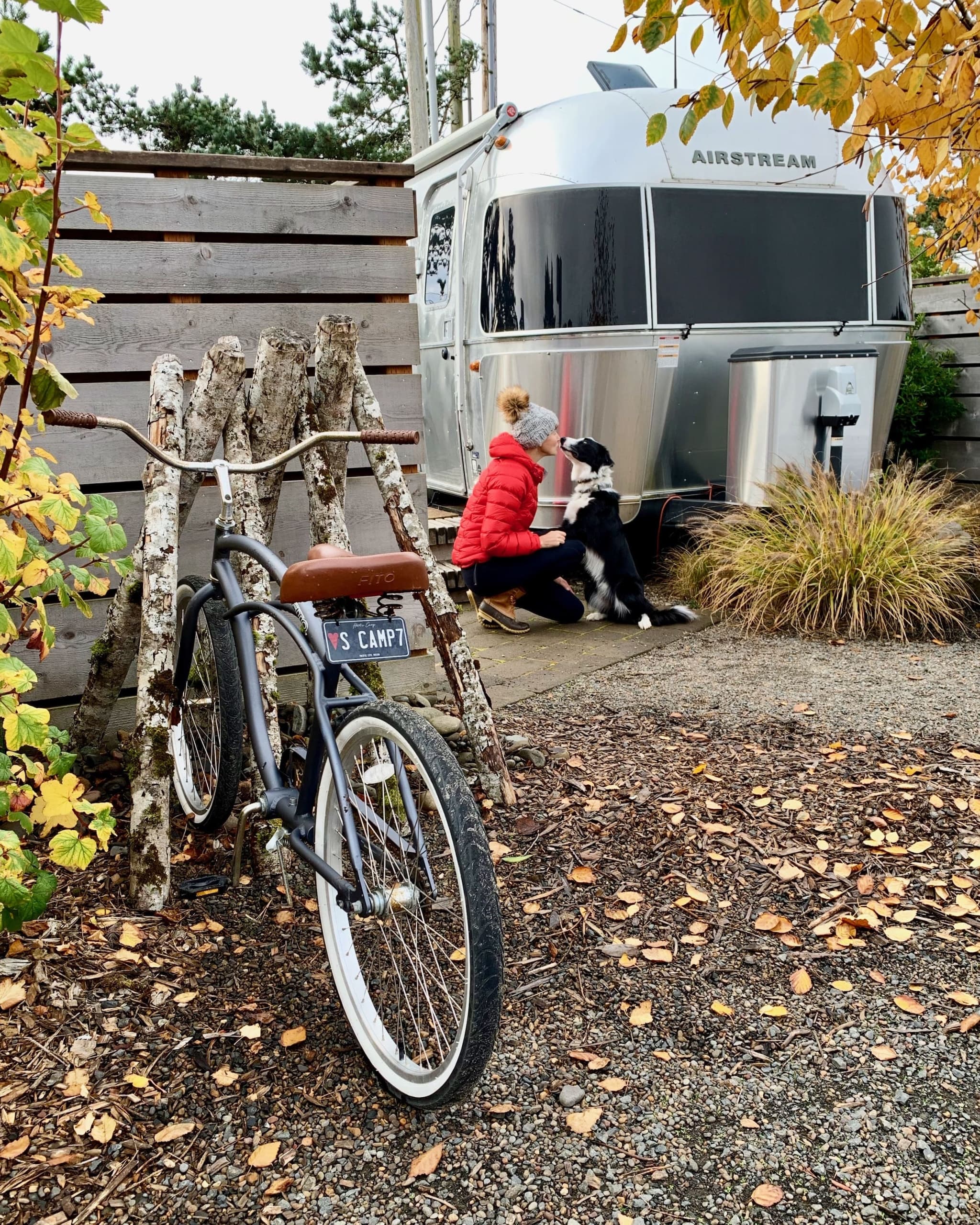 A woman crouching down to give her dog a kiss out front of an Airstream at Harts Camp
