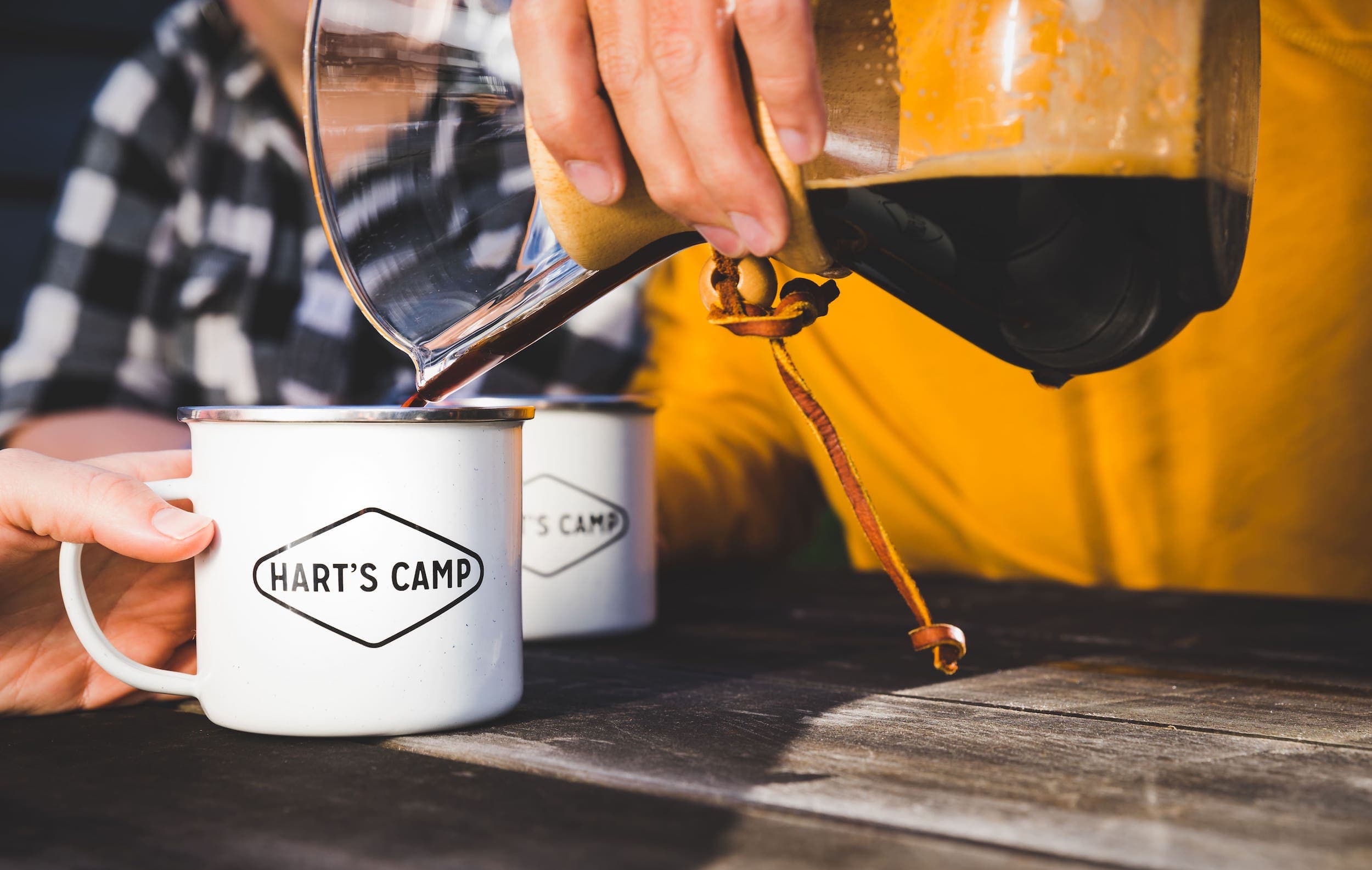 2 Harts Camp mugs on a picnic table with someone pouring pour over coffee into them at Harts Camp Campground