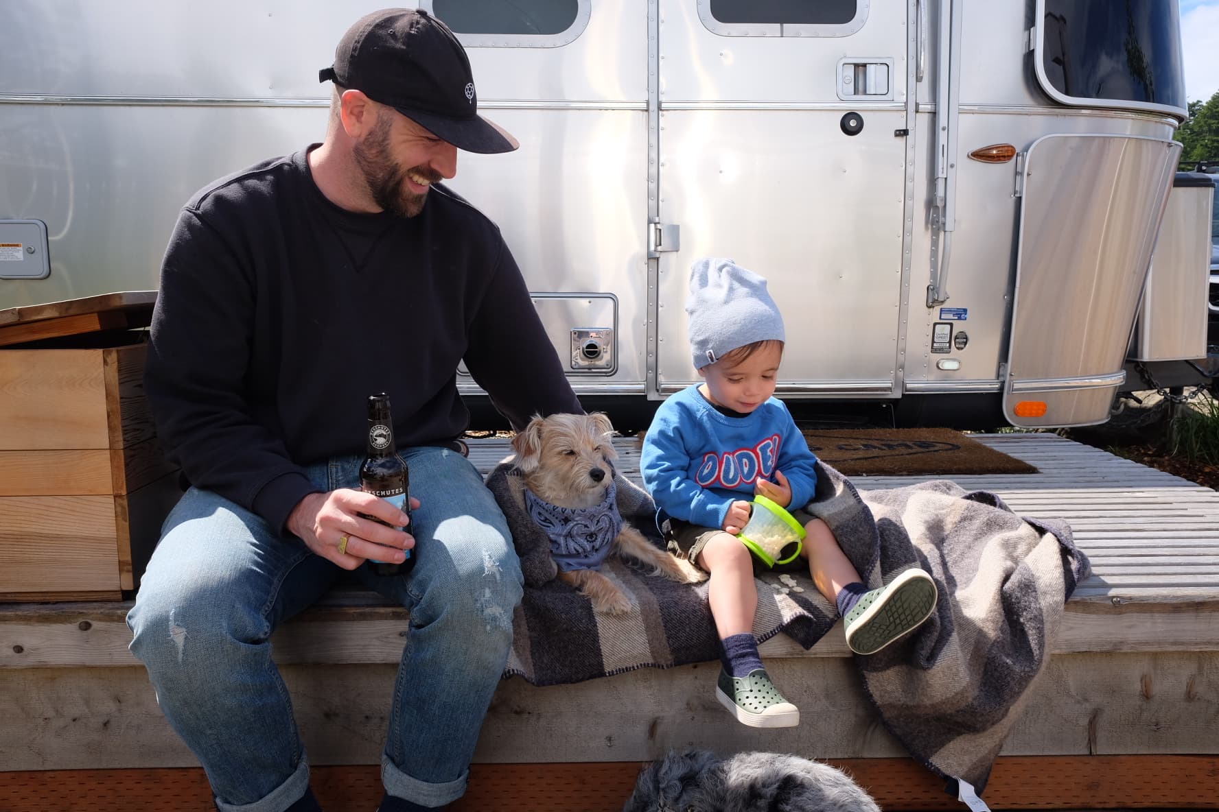 A father , dog, and child sitting on the deck of an airstream at Harts Camp