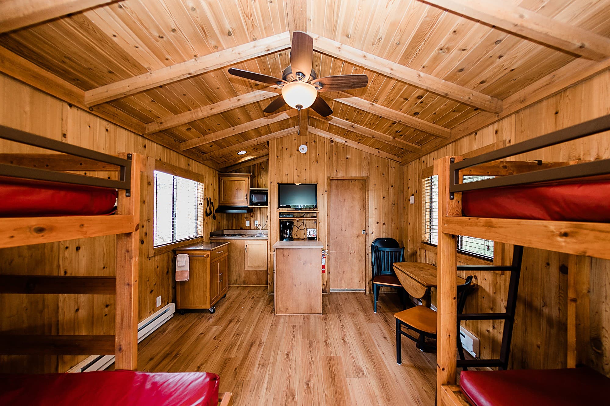 Full interior of a deluxe sleeper cabin with bunk beds, ceiling fan and kitchenette at Hart's Camp, Pacific City, Oregon