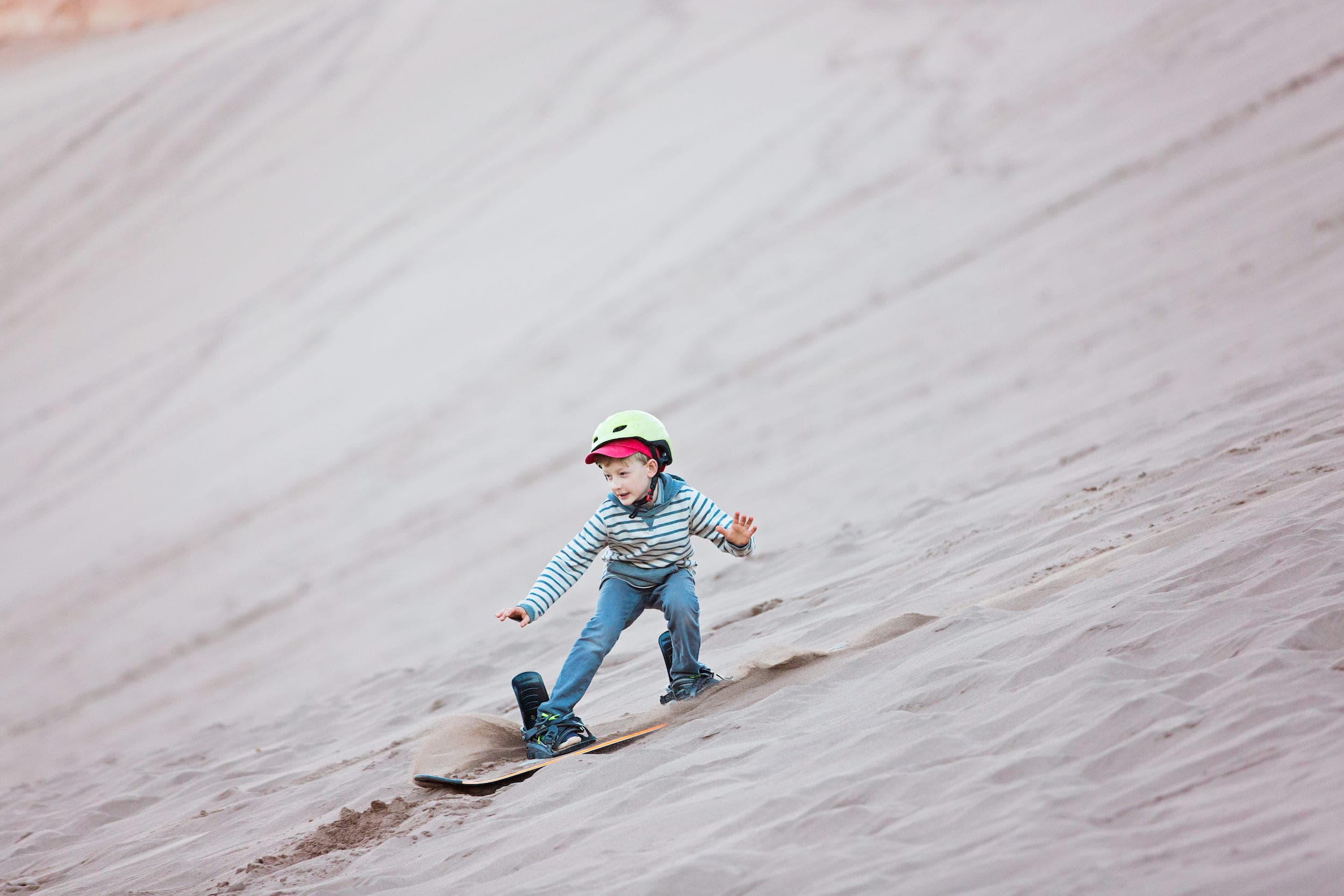 A boy gliding down a sand dune on a sand board at Cape Kiwanda