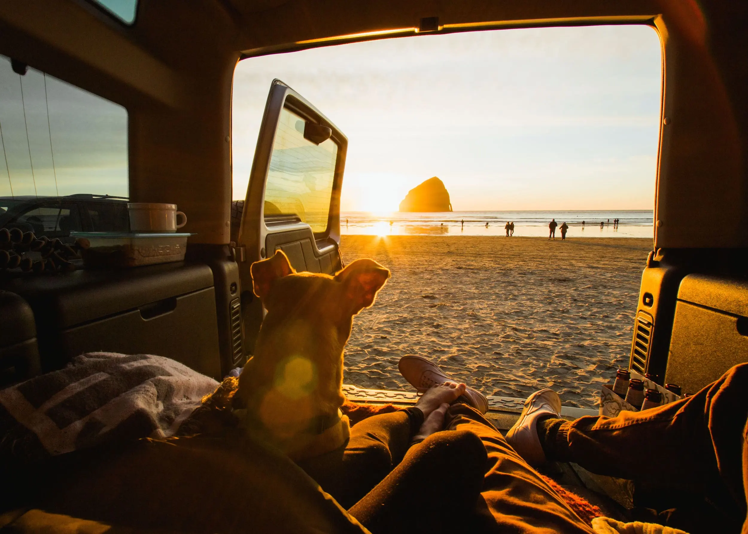 A dog and two people sitting in the back of a van on the beach looking out to the ocean at sunset at Cape Kiwanda