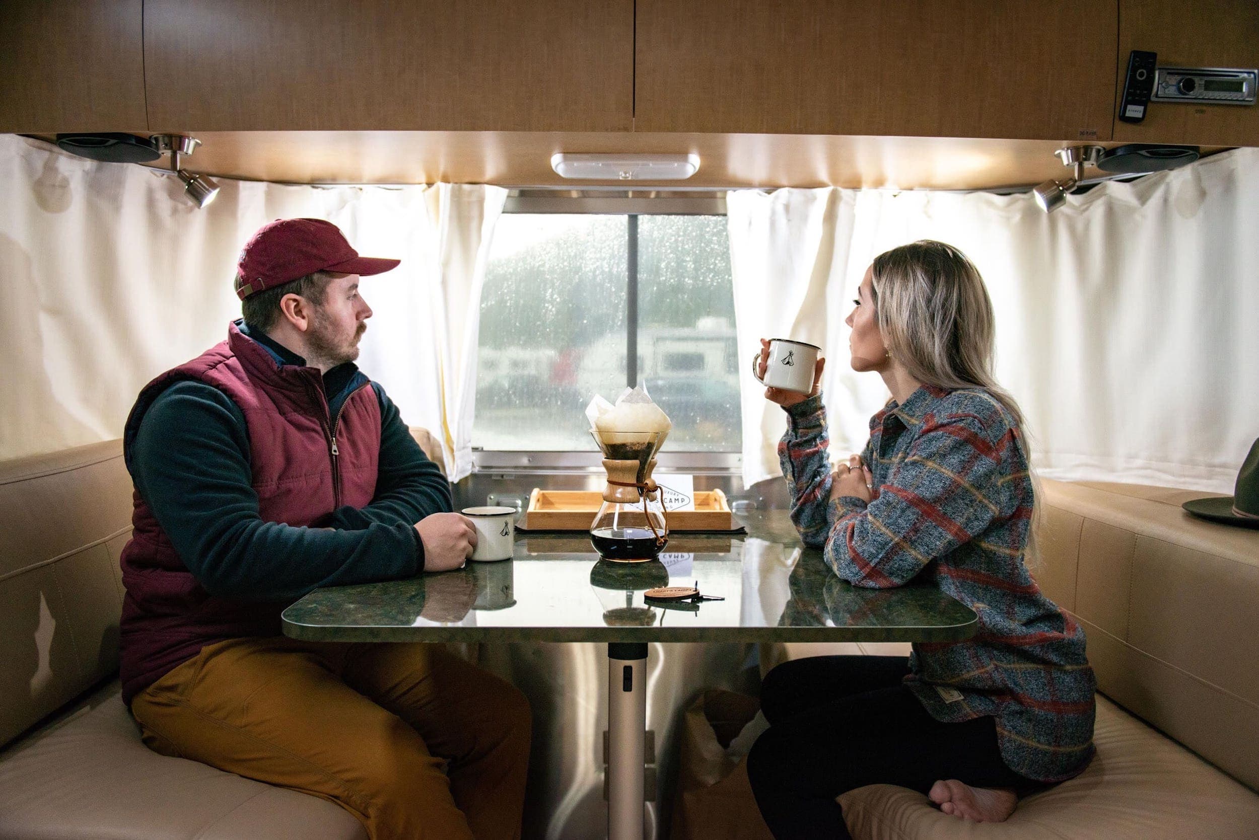A couple sitting at a table inside an airstream drinking coffee on a rainy day