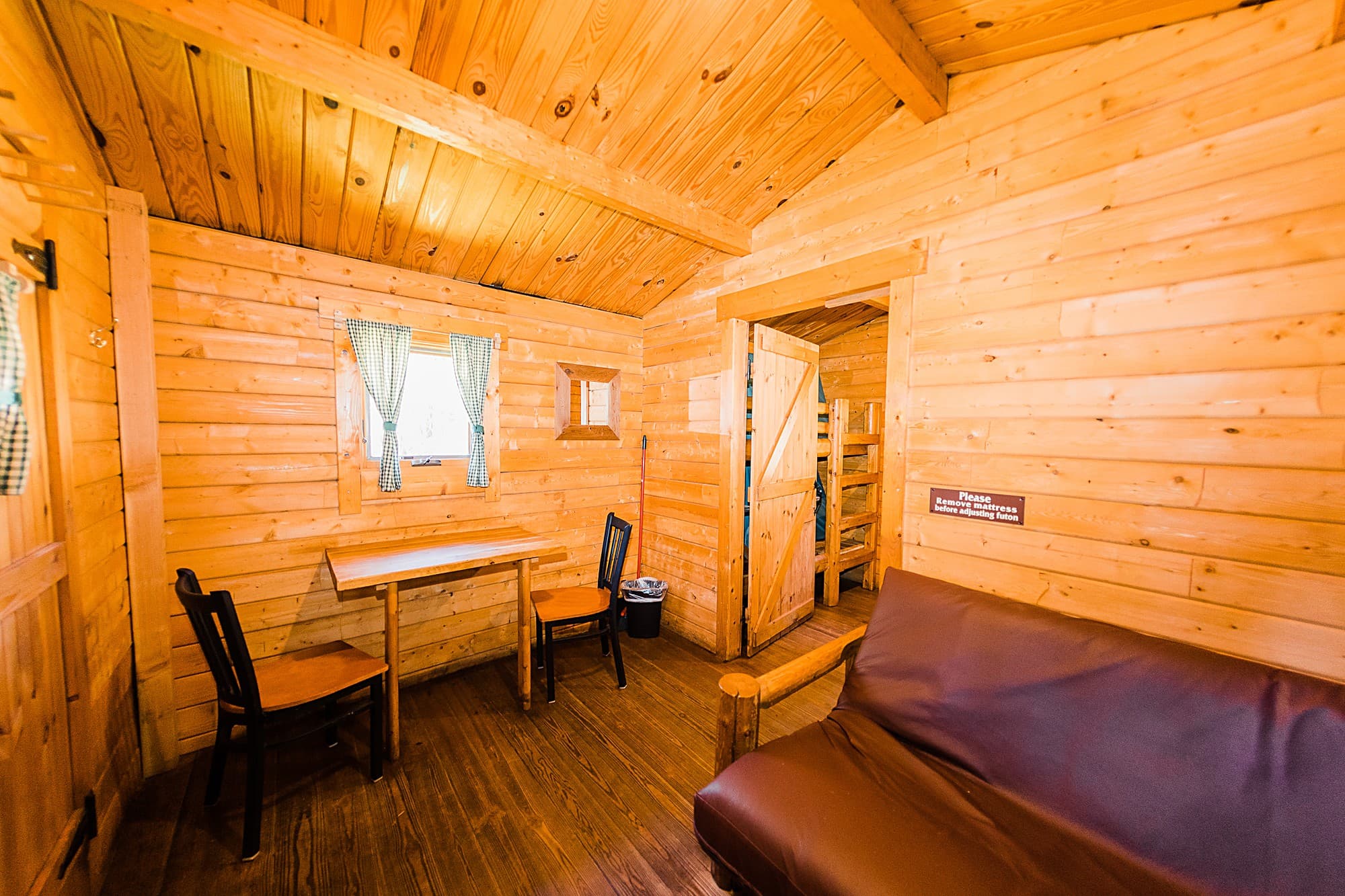 Interior of a one-bedroom camping cabin at The Inn at Hart's Camp in Pacific City, Oregon, with pine walls, a dining table and a futon