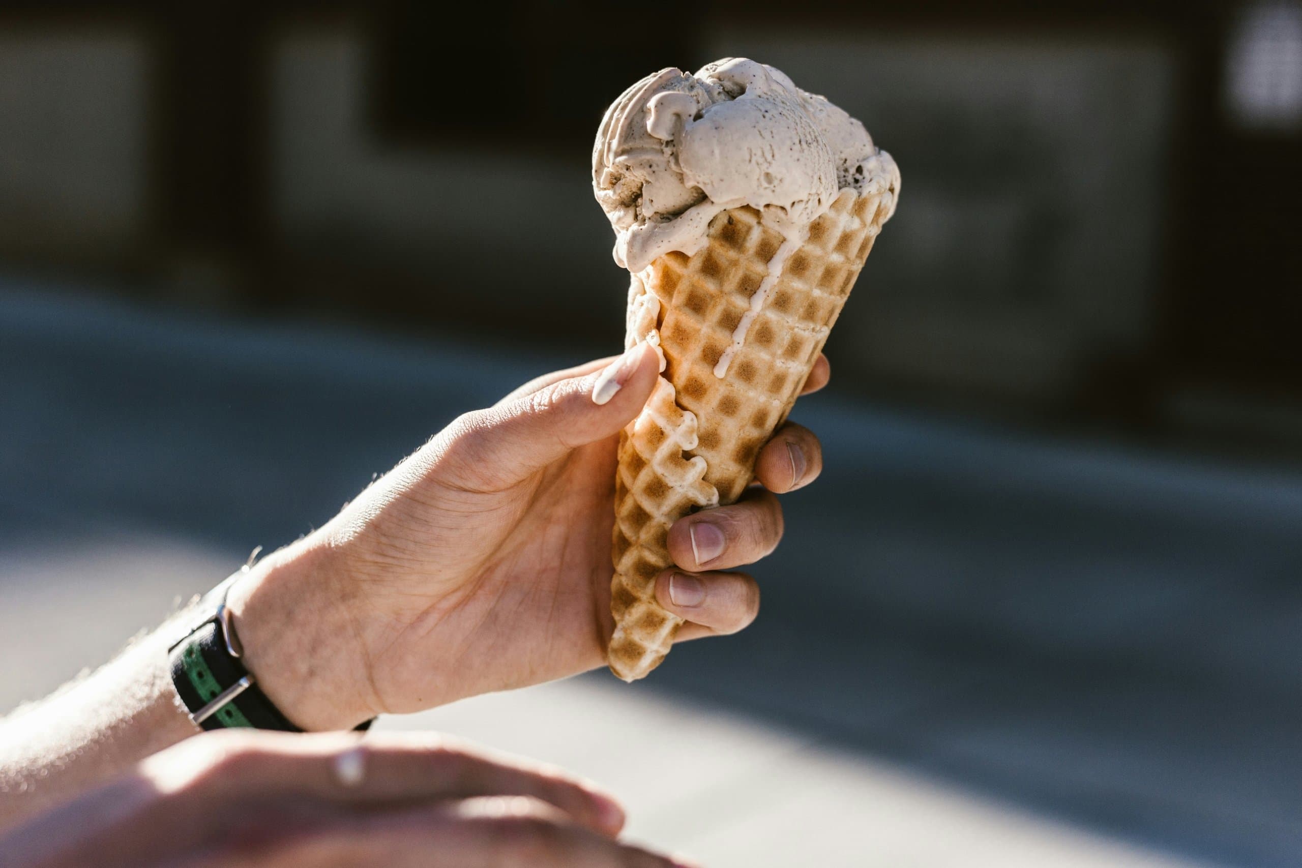 a hand holding a drippy ice cream in a waffle cone.