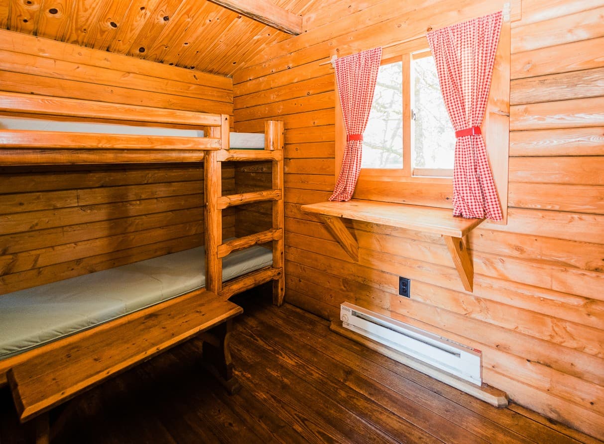 Wooden bunk beds with red gingham curtains inside a studio camping cabin near Cape Kiwanda on the Oregon Coast