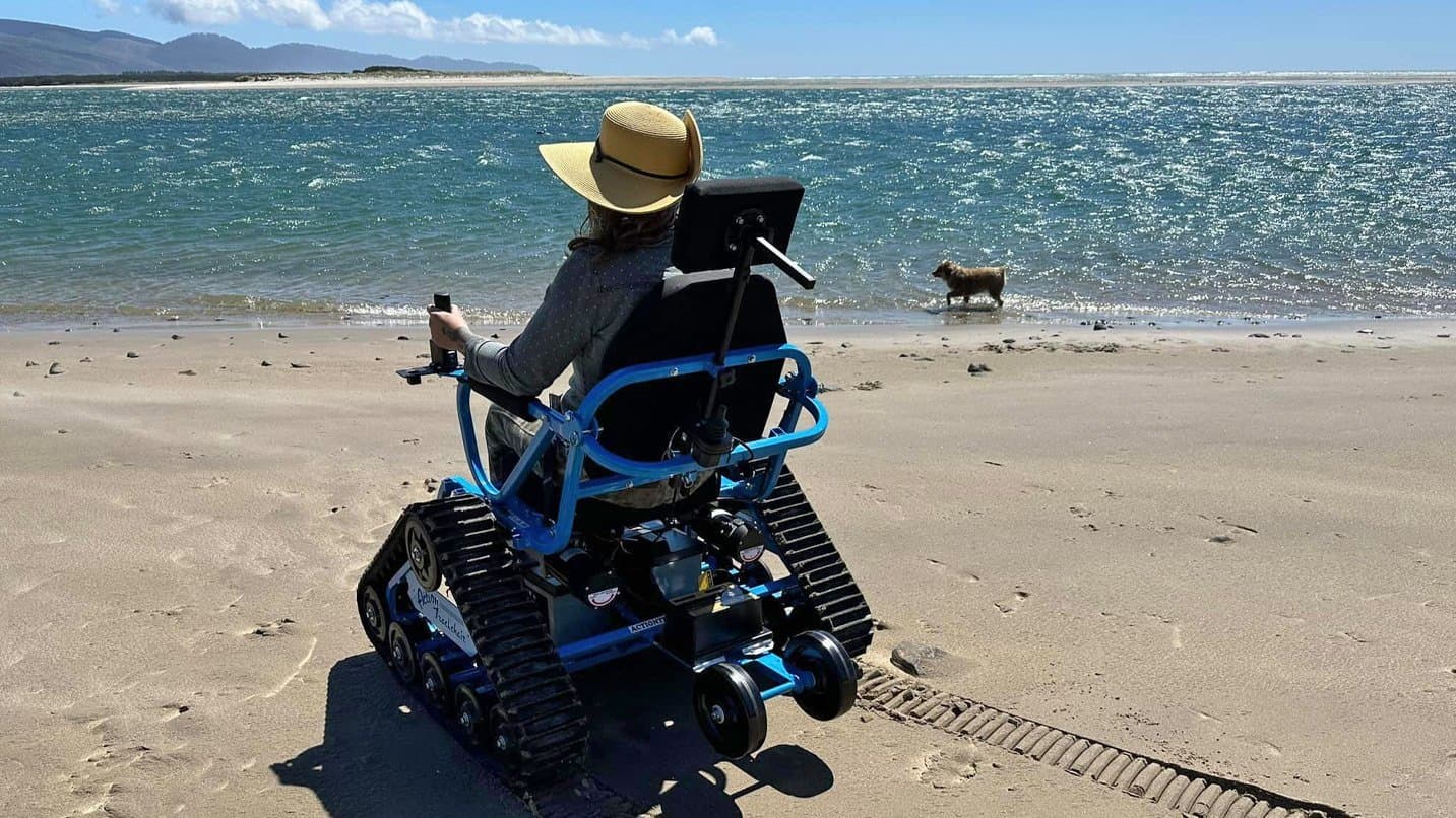 A woman on her electric all-terrain chair on the beach with her dog