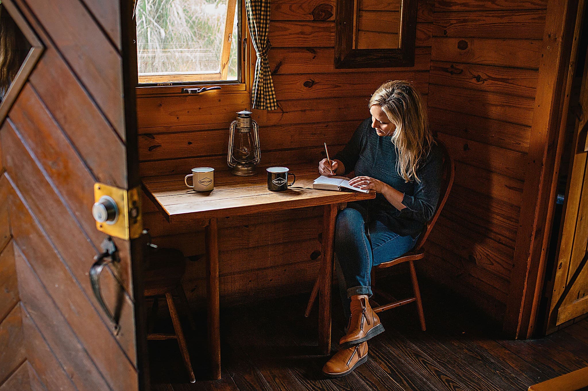 Guest journaling with coffee in Hart's Camp mugs inside a cozy wood cabin at The Inn at Hart's Camp, an Oregon Coast glamping resort