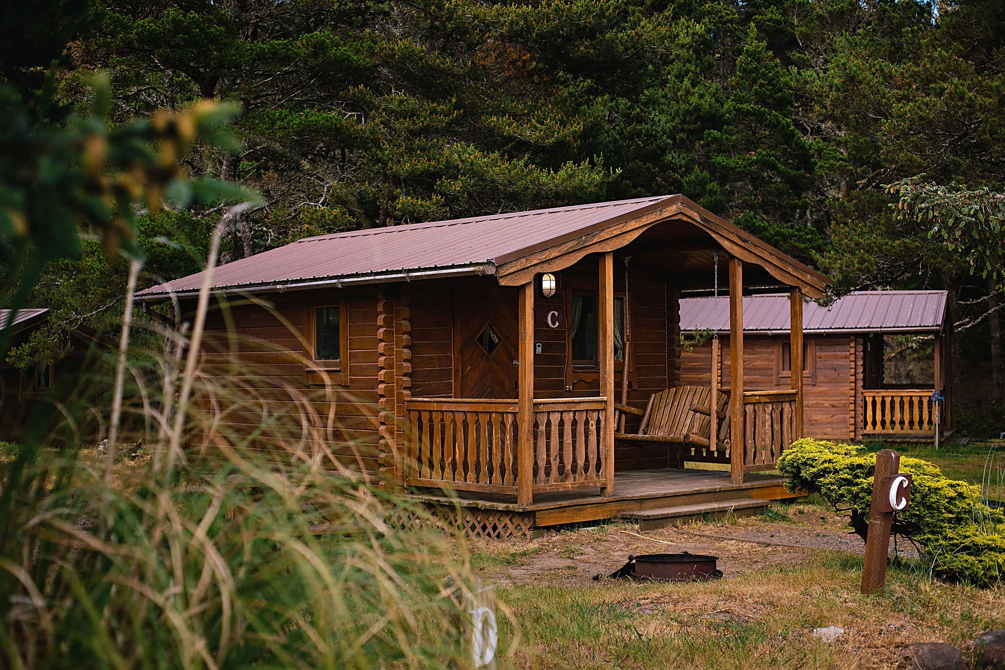 Rustic camping cabin with covered porch swing and fire pit surrounded by shore pines at The Inn at Hart's Camp in Pacific City