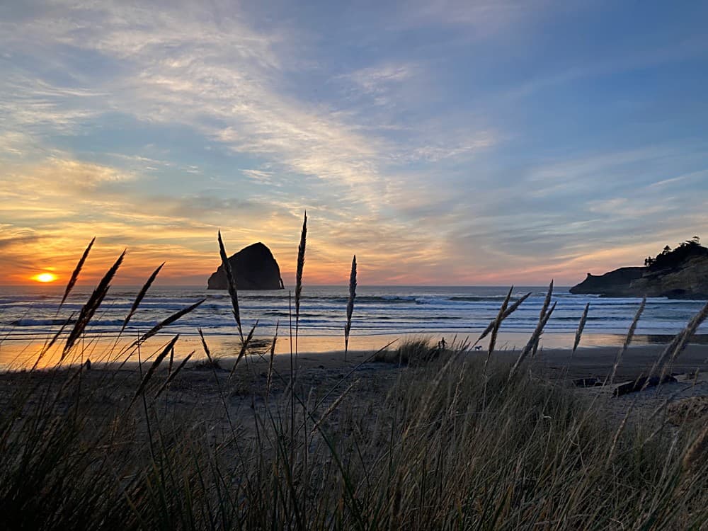 Sunset over Haystack Rock and the beach at Cape Kiwanda, framed by dune grass near The Inn at Hart's Camp in Pacific City, Oregon