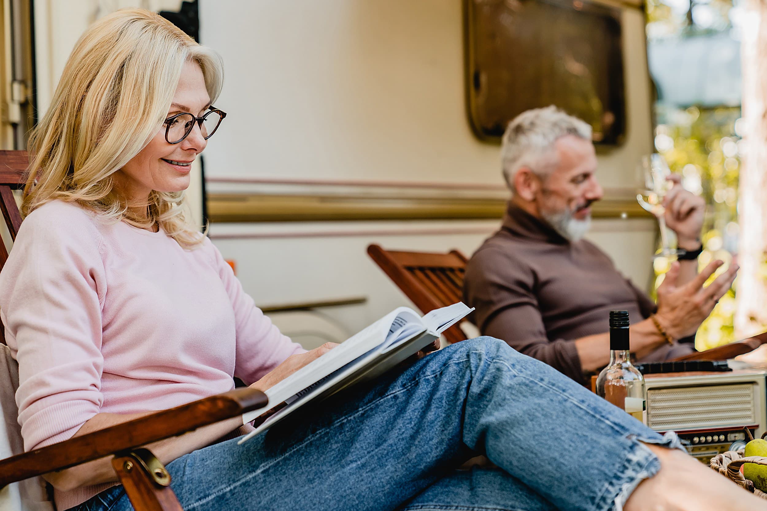 Mature couple relaxing outside their RV with a book and glass of wine at The Inn at Hart's Camp, an RV resort in Pacific City, Oregon Coast.