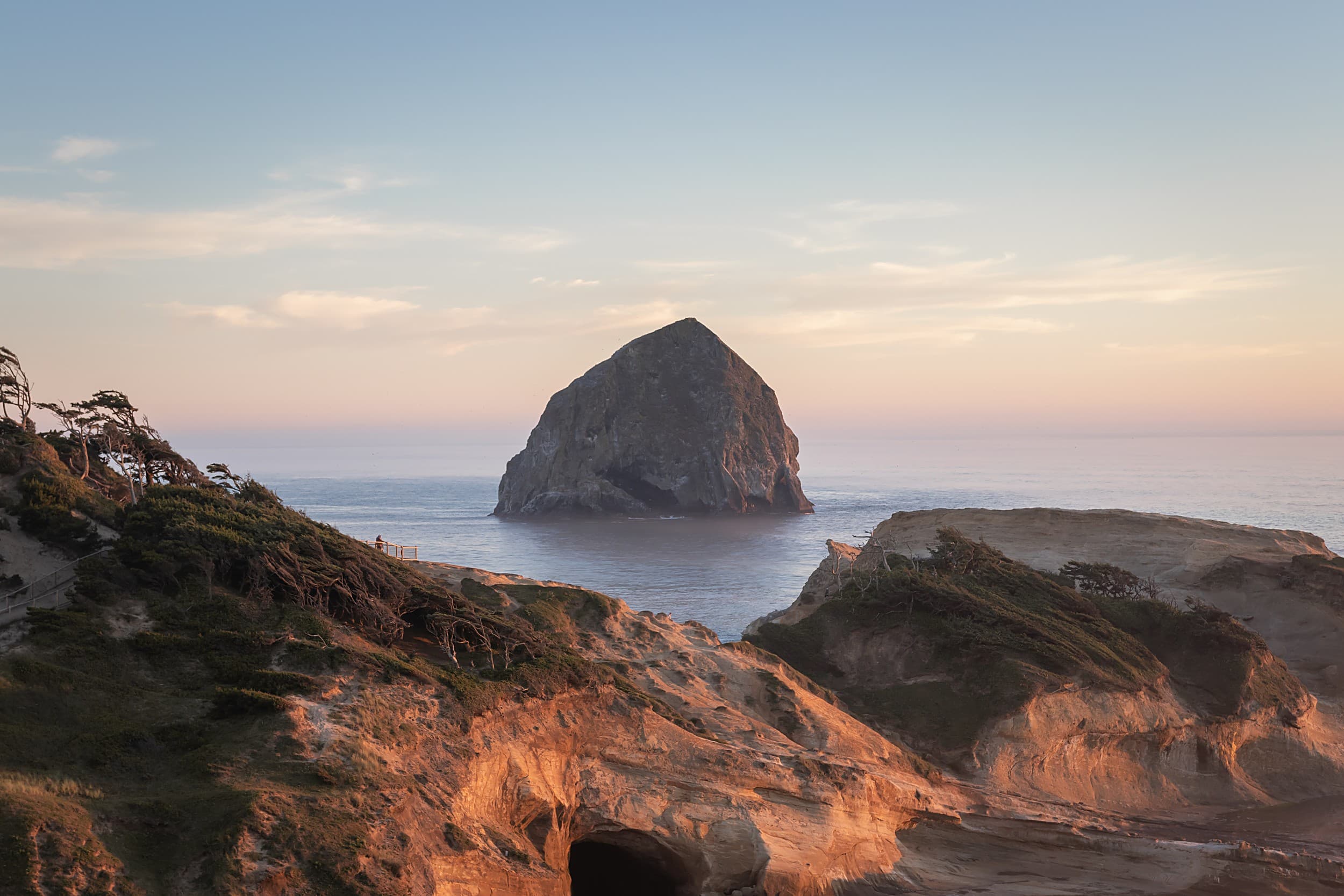 Haystack Rock rising offshore at sunset near sandstone cliffs on the Oregon Coast